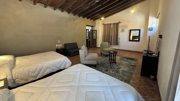 Habitación de hotel con dos camas, un sofá, una silla, una mesita y un televisor.