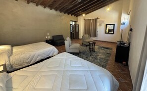 Habitación de hotel con dos camas, un sofá, una silla, una mesita y un televisor.