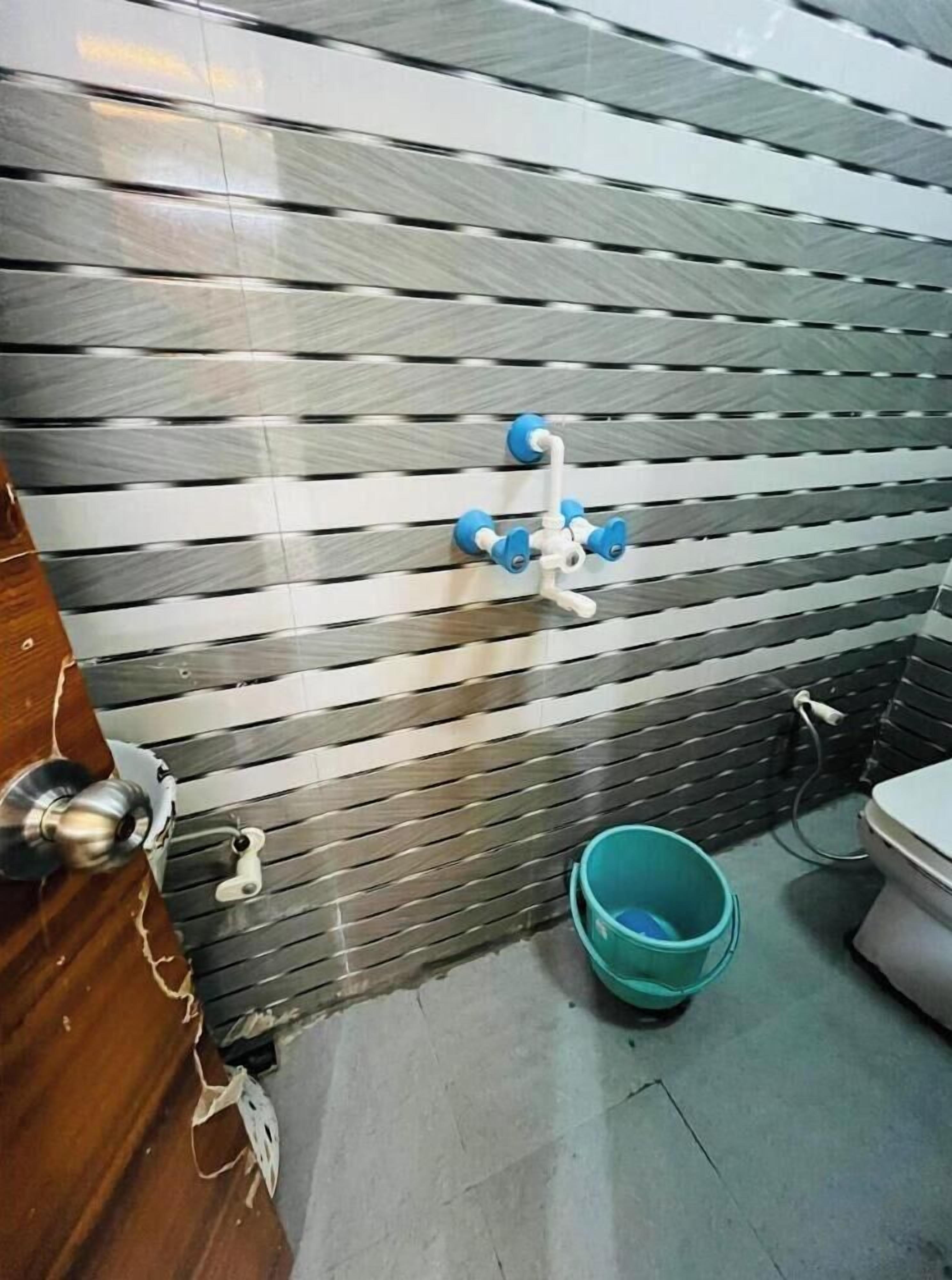 A bathroom with a striped wall, a blue bucket, and a toilet.