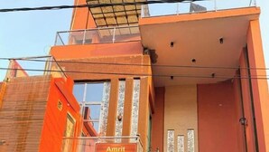 Un immeuble à plusieurs étages, sur lequel on peut lire l’inscription « Amrit Residency ». Il est doté d’un escalier, d’une entrée fermée par un portail et d’un balcon.