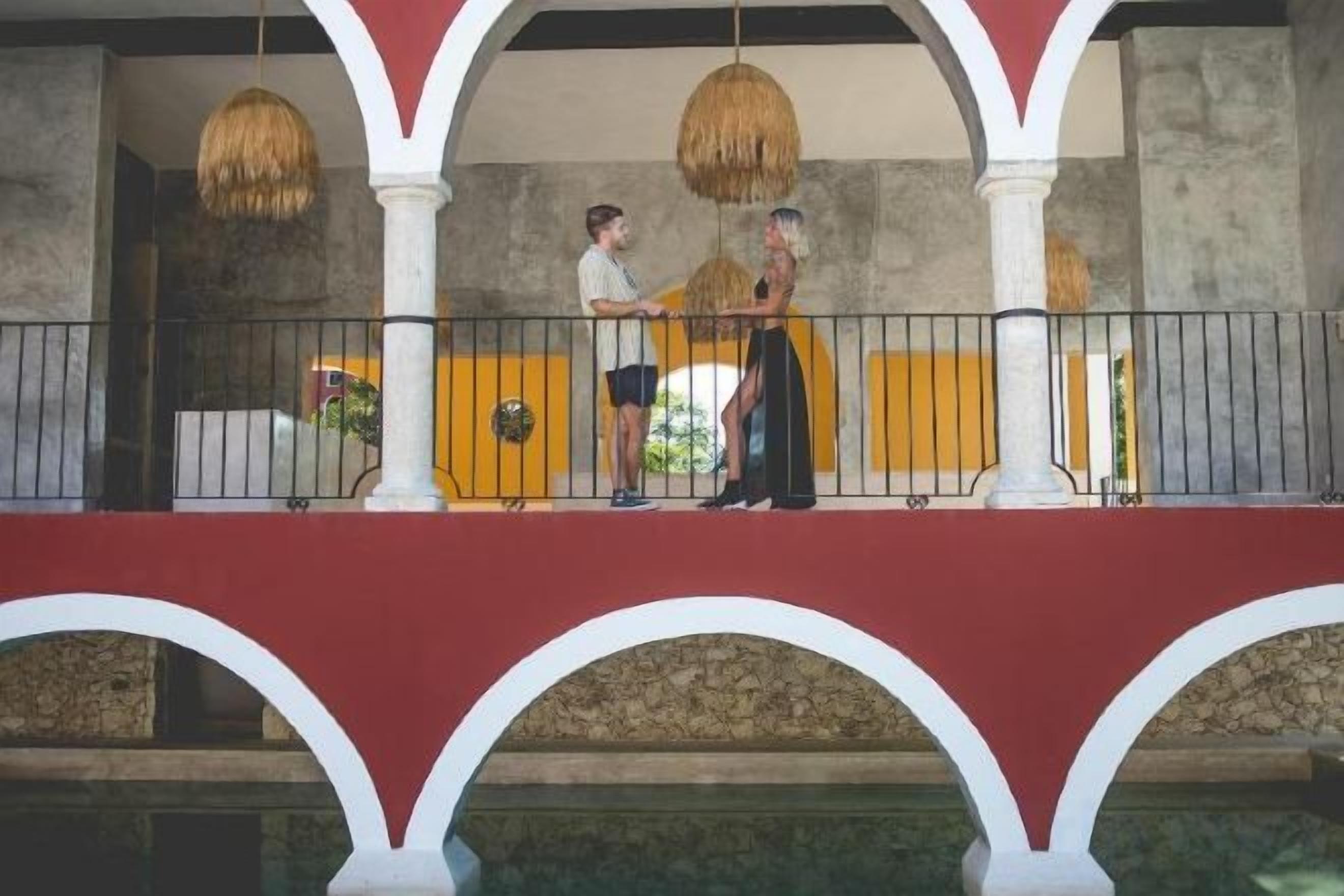 A balcony with a railing, a person standing, and another person sitting.