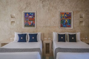 Two beds with white linens and blue pillows, a textured beige wall, and two framed artworks. - Wakax Hacienda - Cenote & Boutique Hotel (Tulum)