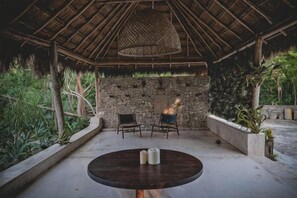 An outdoor seating area with a round table, two chairs, and a stone wall backdrop. - Wakax Hacienda - Cenote & Boutique Hotel (Tulum)