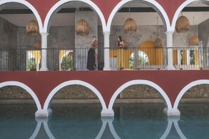 A pool area with a reflection, a balcony with a railing, and a person standing. - Wakax Hacienda - Cenote & Boutique Hotel (Tulum)