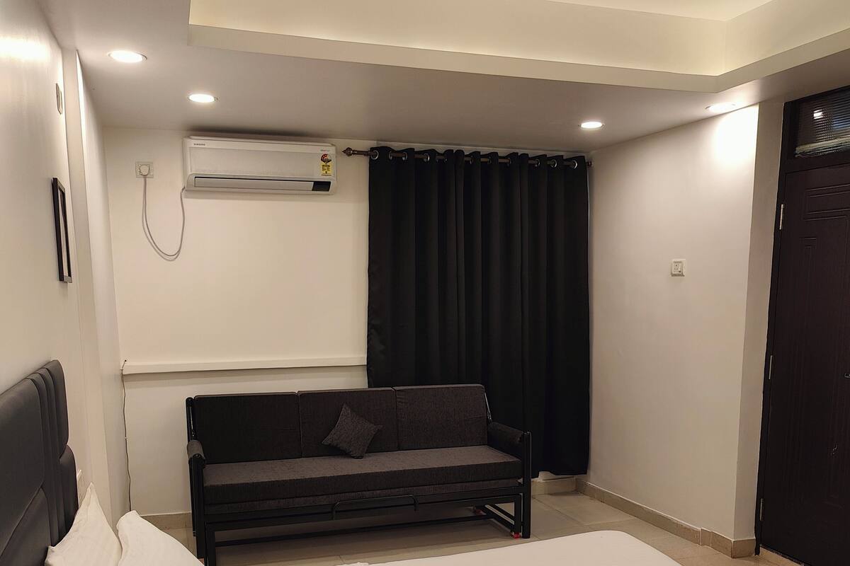 A modern hotel room with a large bed, a sofa, and an air conditioning unit on the wall.