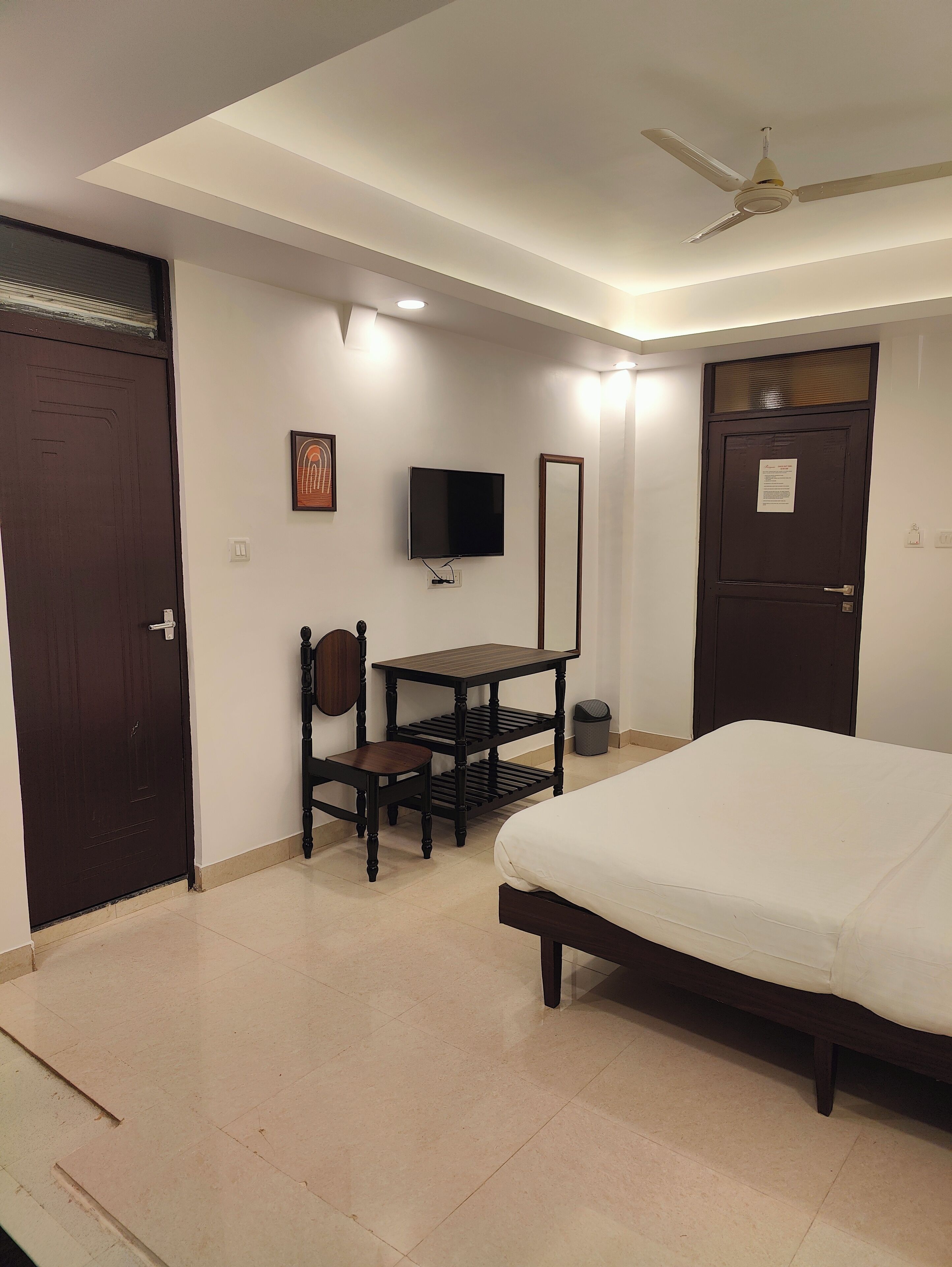 A bedroom with a bed, a desk, a chair, a TV, and a ceiling fan.