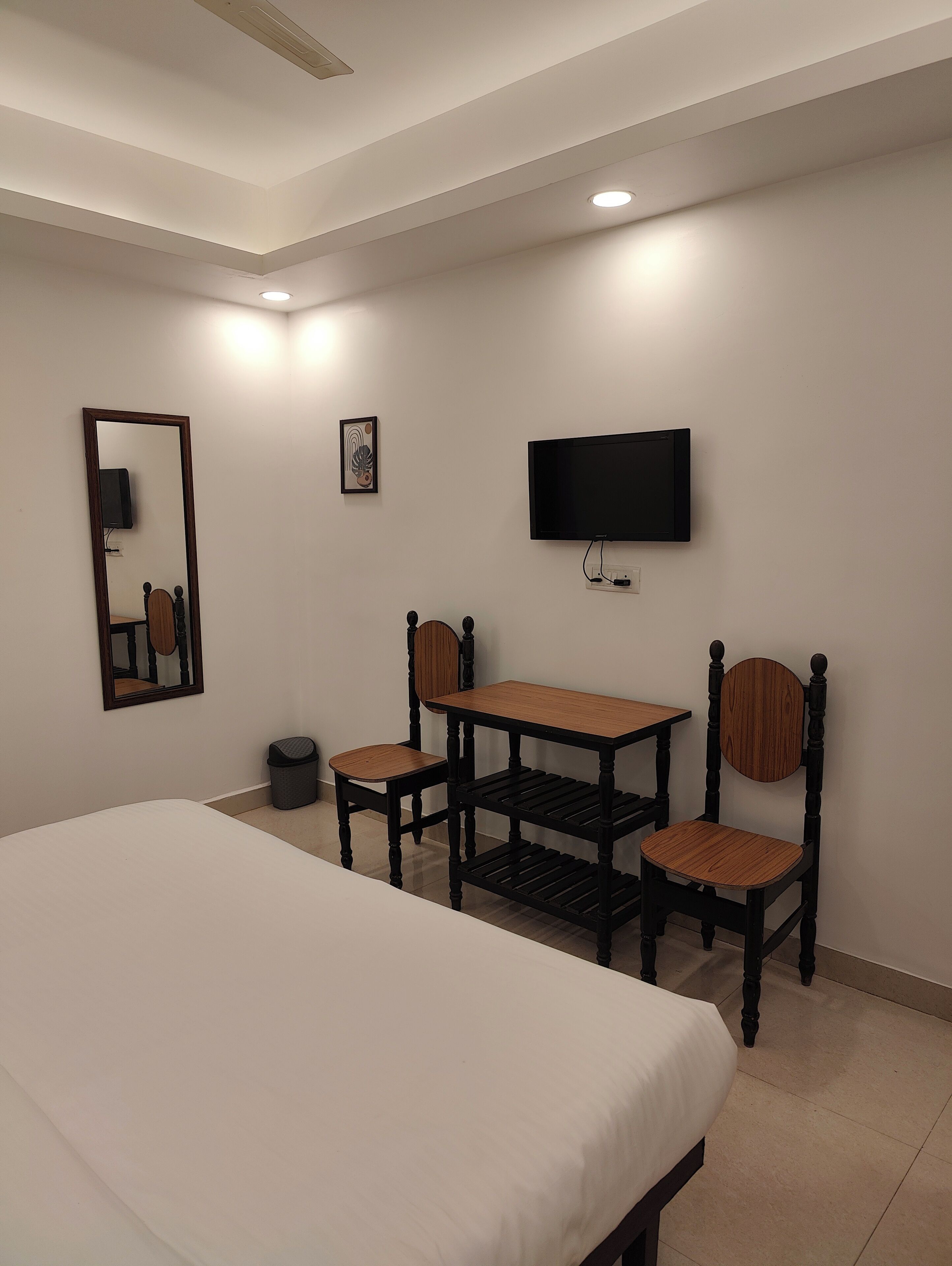 Habitación de hotel con cama, escritorio, dos sillas, televisor y un pequeño cubo de basura.
