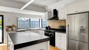 A modern kitchen with a central island, stainless steel appliances, and a large window providing natural light. - Queenstown Family Base, 100m to the Lake (Queenstown)