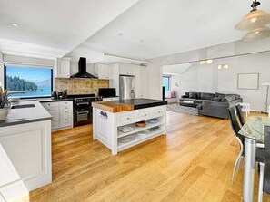 A modern kitchen with white cabinetry, a central island, and a view of a lake. - Queenstown Family Base, 100m to the Lake (Queenstown)