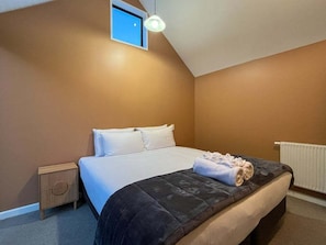 Ein Schlafzimmer mit einem Bett, einem Nachttisch, einem Fenster und einer Deckenleuchte.