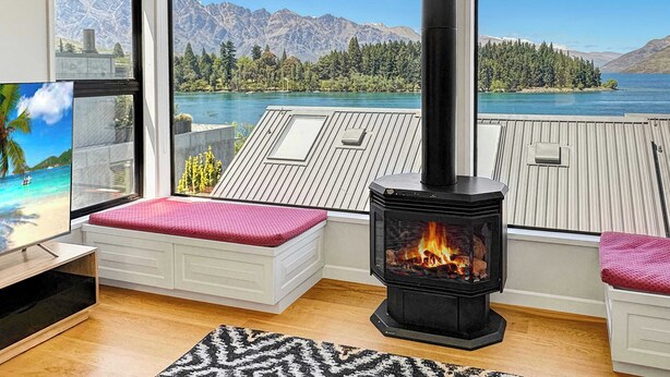 A modern living room with a large window, a fireplace, and a view of a lake and mountains. - Queenstown Family Base, 100m to the Lake (Queenstown)