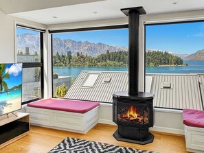 A modern living room with a large window, a fireplace, and a view of a lake and mountains. - Queenstown Family Base, 100m to the Lake (Queenstown)