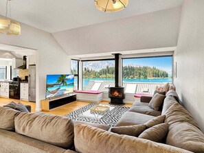 A modern living room with a sofa, a flat-screen TV, a fireplace, and a view of a lake and mountains. - Queenstown Family Base, 100m to the Lake (Queenstown)