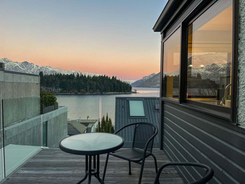 A balcony with a table and chairs overlooking a lake and mountains.