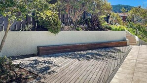 A wooden deck with a built-in bench, surrounded by greenery and a white wall. - Queenstown Family Base, 100m to the Lake (Queenstown)