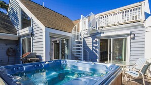 A hot tub on a wooden deck, a covered patio with chairs, and a house with a balcony. - Private Access to Beach Boardwalk 4; FREE Amenity Card Privileges; Back Deck w/ Private Hot Tub! (Seabrook Island)