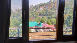 Blick aus einem Fenster mit Metallgeländer auf einen Hügel mit Gebäuden und Grünflächen.