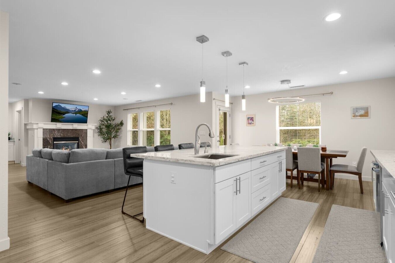 A modern kitchen with white cabinets, a central island, a dining area with a table and chairs, and a gray sofa in a living room.