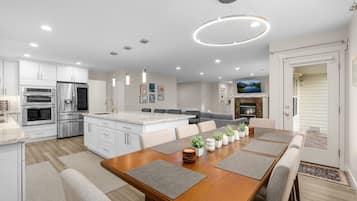 A modern kitchen with built-in appliances, a dining area with a wooden table and chairs, and a living room with a fireplace and a television.