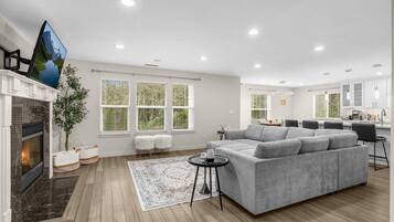 A modern living room with a fireplace, grey sofa, and large windows.