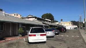 A row of parked cars in a parking lot with buildings in the background. - Commodore motel (Oakland)