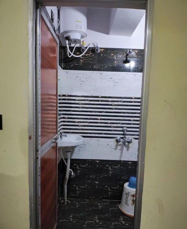 Une salle de bain avec un lavabo blanc, des carreaux de marbre noir et un chauffe-eau.