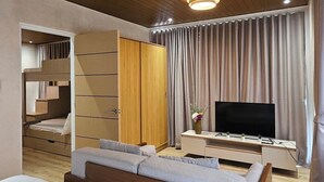 A modern hotel room with a large bed, a TV, a wooden wardrobe, and a desk with a vase of flowers. - Villa Sorrento by SMS Hospitality (San Antonio)