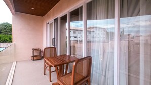 A balcony with a wooden table and two wicker chairs, large sliding glass doors, and a view of buildings in the background. - Villa Sorrento by SMS Hospitality (San Antonio)