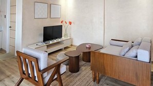 A modern living room with a wooden ceiling, a sofa, a coffee table, a TV, and a small side table with a vase of flowers. - Villa Sorrento by SMS Hospitality (San Antonio)