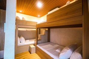 Une chambre avec un lit superposé, des murs et un plafond en bois, une petite table de chevet et un miroir.