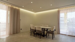 A modern dining area with a round table and six chairs, large windows with sheer curtains, and recessed ceiling lighting. - Elegant Glyfada Residence • 2BR Master • High-End Finishes • Prime Location (Glifada)