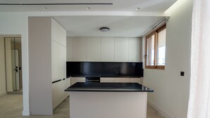 A modern kitchen with white cabinets, a black countertop, and a window with wooden frames. - Elegant Glyfada Residence • 2BR Master • High-End Finishes • Prime Location (Glifada)
