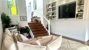 Un salon avec un canapé, un escalier, une bibliothèque et un téléviseur.