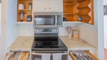 Una cocina compacta con estufa, horno, microondas y batidora integrada. Hay estantes de madera sobre la estufa y un organizador de cuchillos a la derecha.