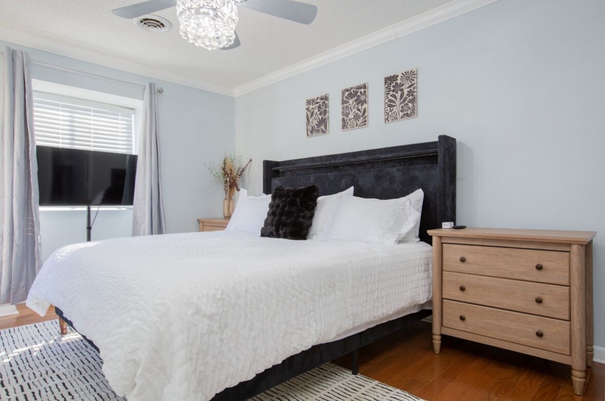 A bedroom with a large bed, a bedside table, a ceiling fan, and decorative wall art.
