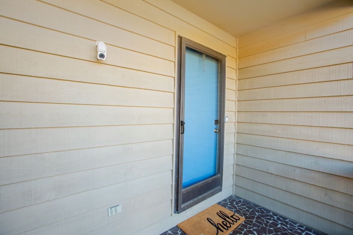 A house entrance with a blue door, a security camera, and a doormat with "hello" written on it.