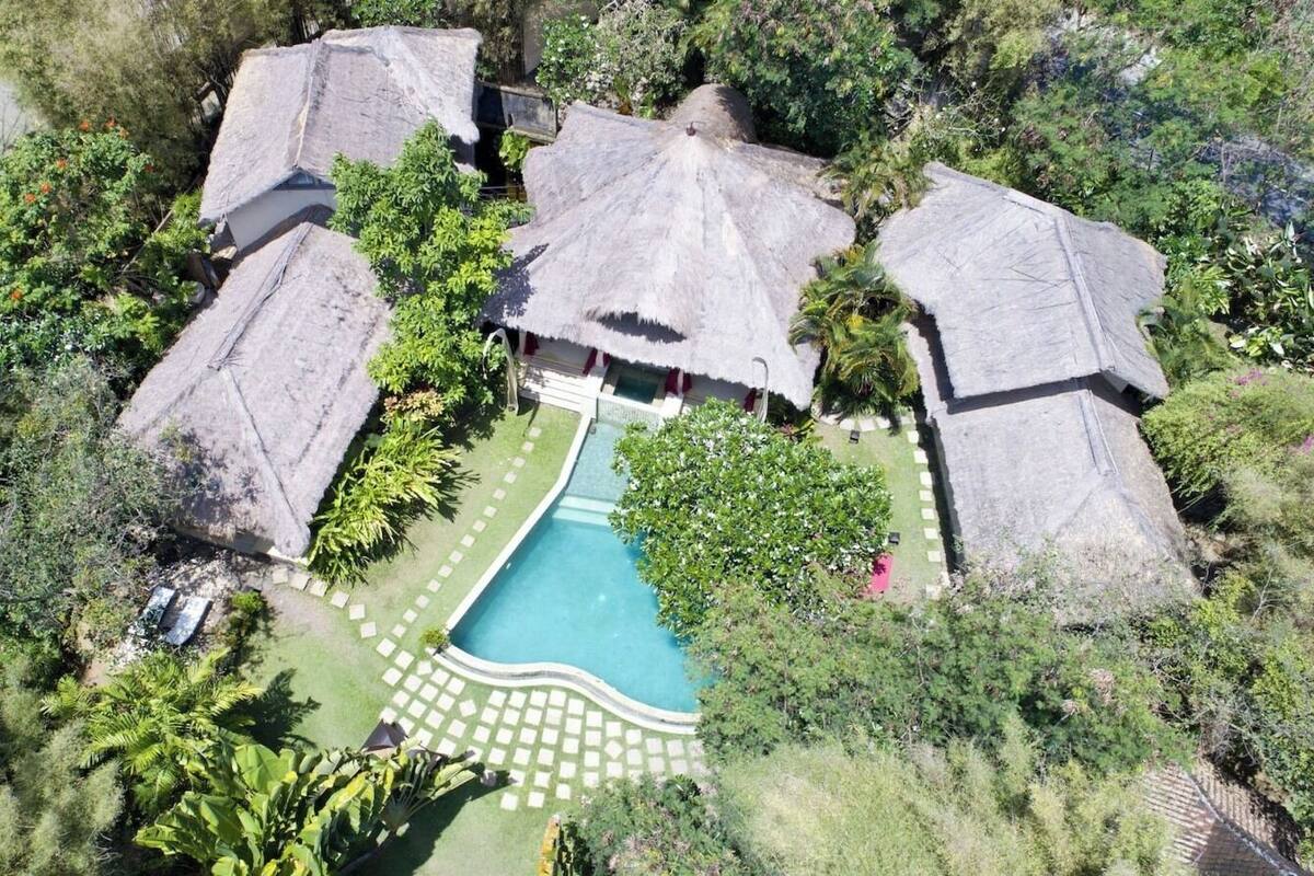 Vue aérienne d’un complexe hôtelier avec des bungalows aux toits de chaume, une piscine et une végétation luxuriante.