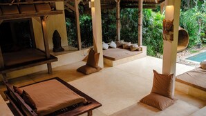 A serene indoor garden with a wooden bench, a cushioned seating area, and a stone floor. - Nomadic Resort Bali (Kerobokan)