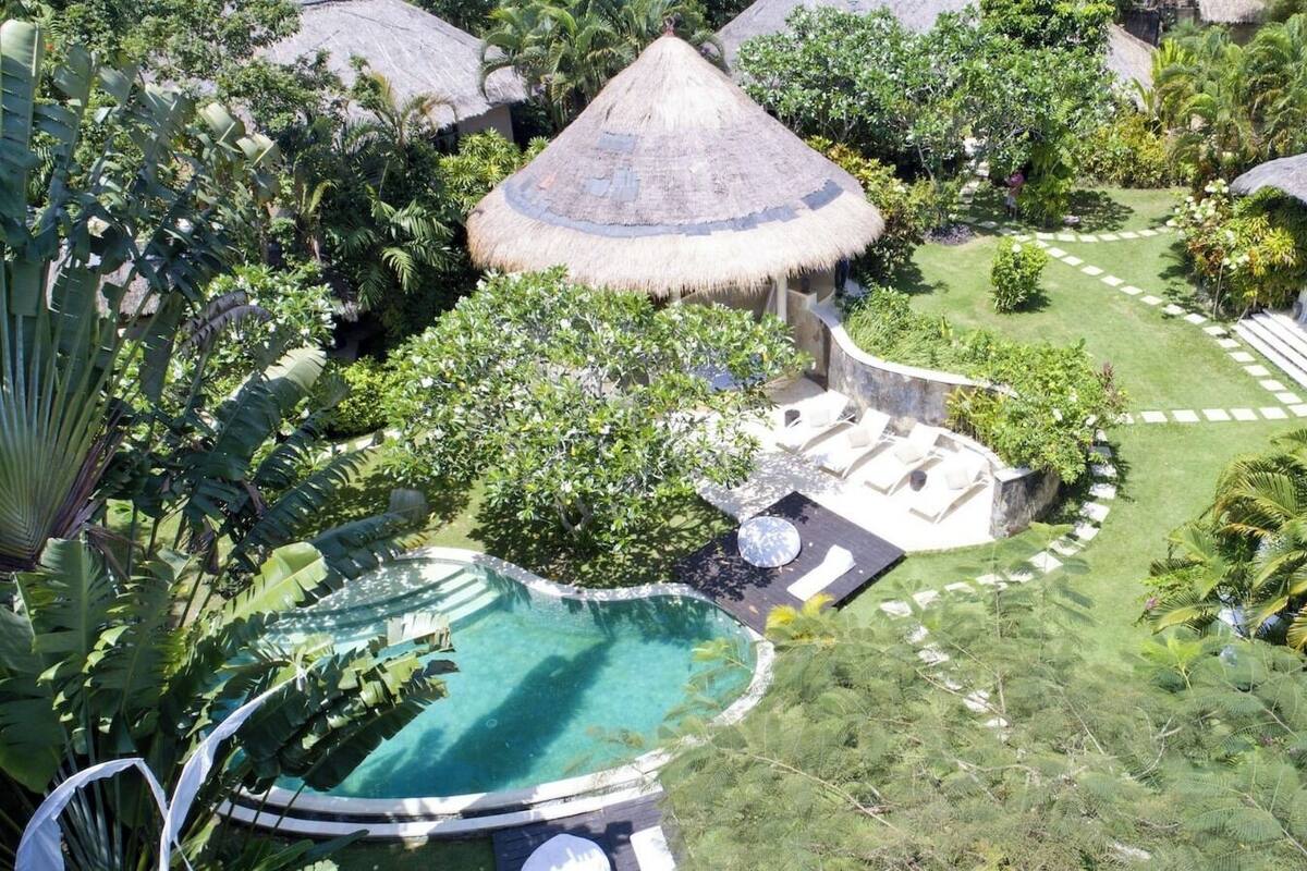 Vue aérienne d’un complexe hôtelier doté d’une piscine, d’espaces de détente et de bâtiments à toits de chaume, le tout au milieu d’une végétation luxuriante.