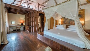 A spacious bedroom with a large bed, wooden floor, and a ladder leading to a loft area. - Nomadic Resort Bali (Kerobokan)