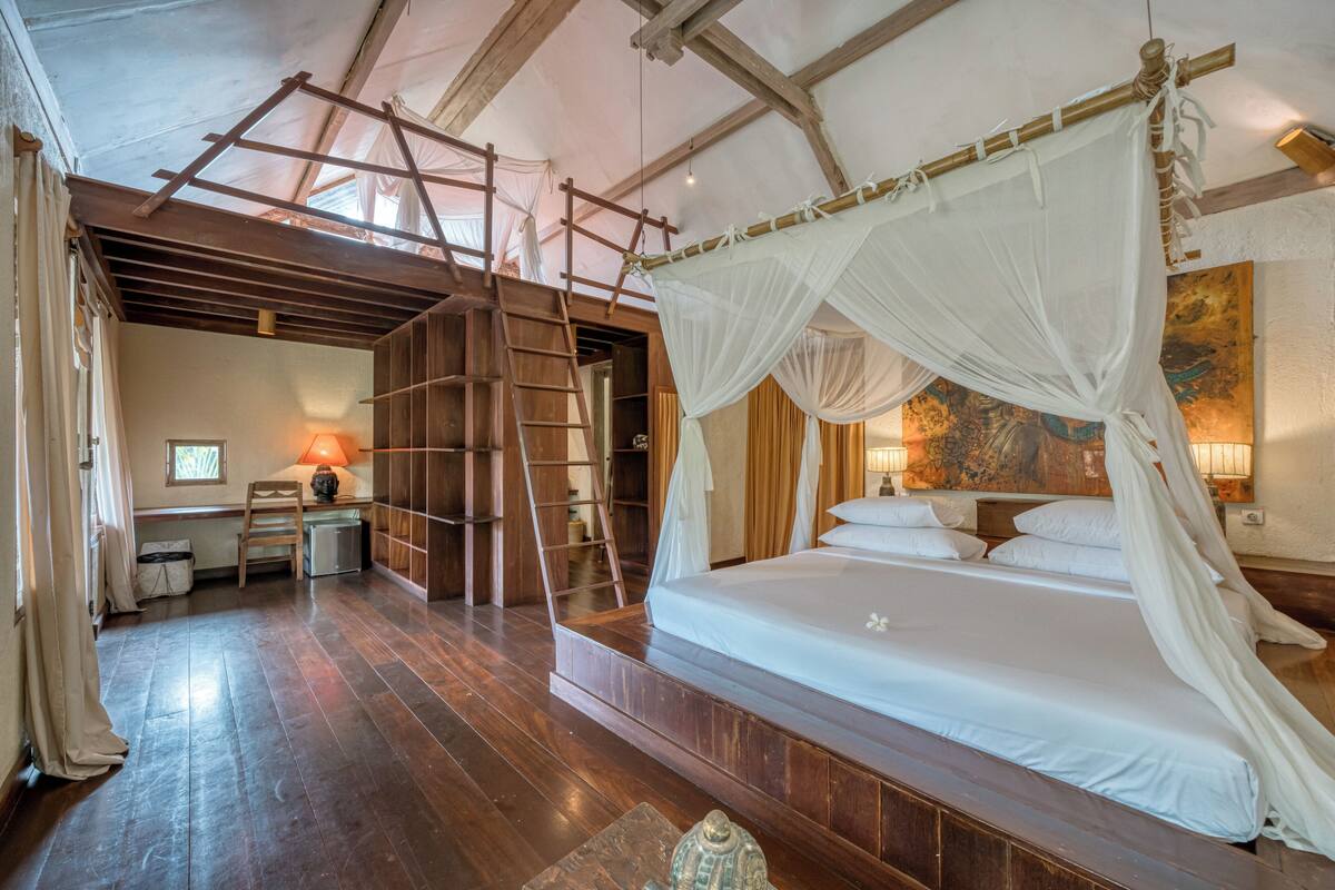 Une chambre spacieuse avec un grand lit, un plancher en bois et une échelle menant à une mezzanine.
