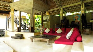 A spacious living area with a red sofa, a coffee table, and a staircase leading to an upper level. - Nomadic Resort Bali (Kerobokan)
