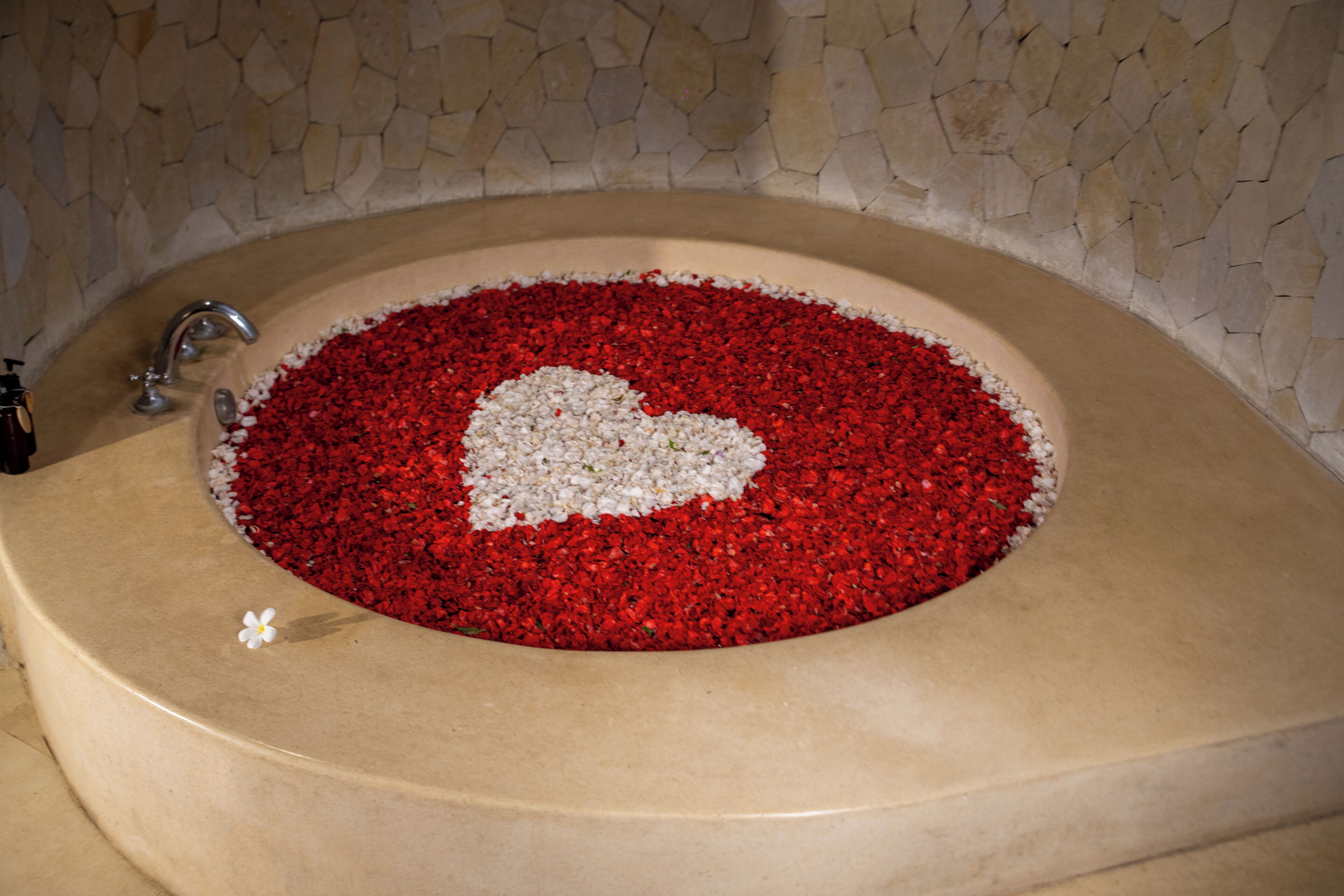 A bathtub filled with red and white bath salts, a white flower, and a heart-shaped arrangement.