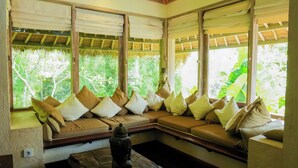 A room with a built-in bench along the window, offering a view of lush greenery outside. - Nomadic Resort Bali (Kerobokan)