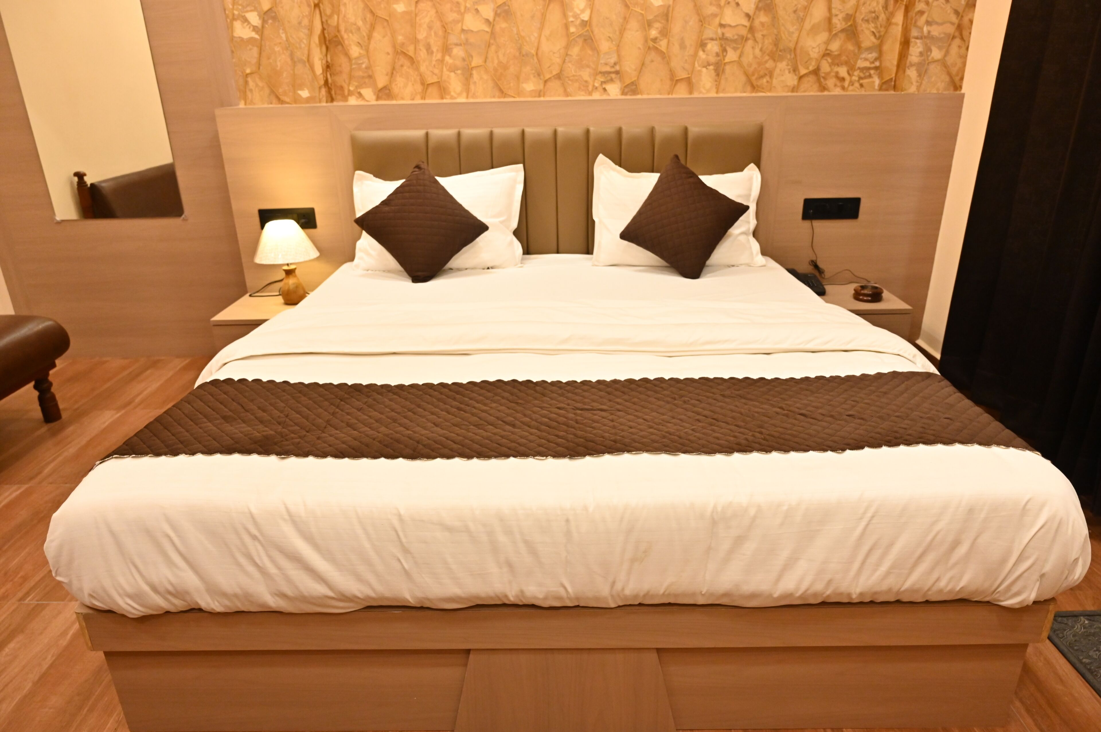 A neatly made bed with a headboard, a bedside lamp, and a nightstand with a phone and a cup.