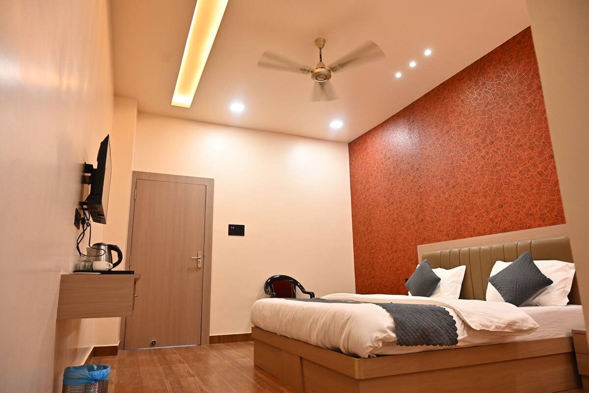 A bedroom with a bed, a ceiling fan, a TV mounted on the wall, and a wooden door.