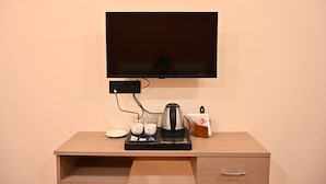 A hotel room with a flat-screen TV mounted on the wall, a coffee maker on a tray table, two cups, and a tissue box. - Hotel Pinaka (Pratapgarh)