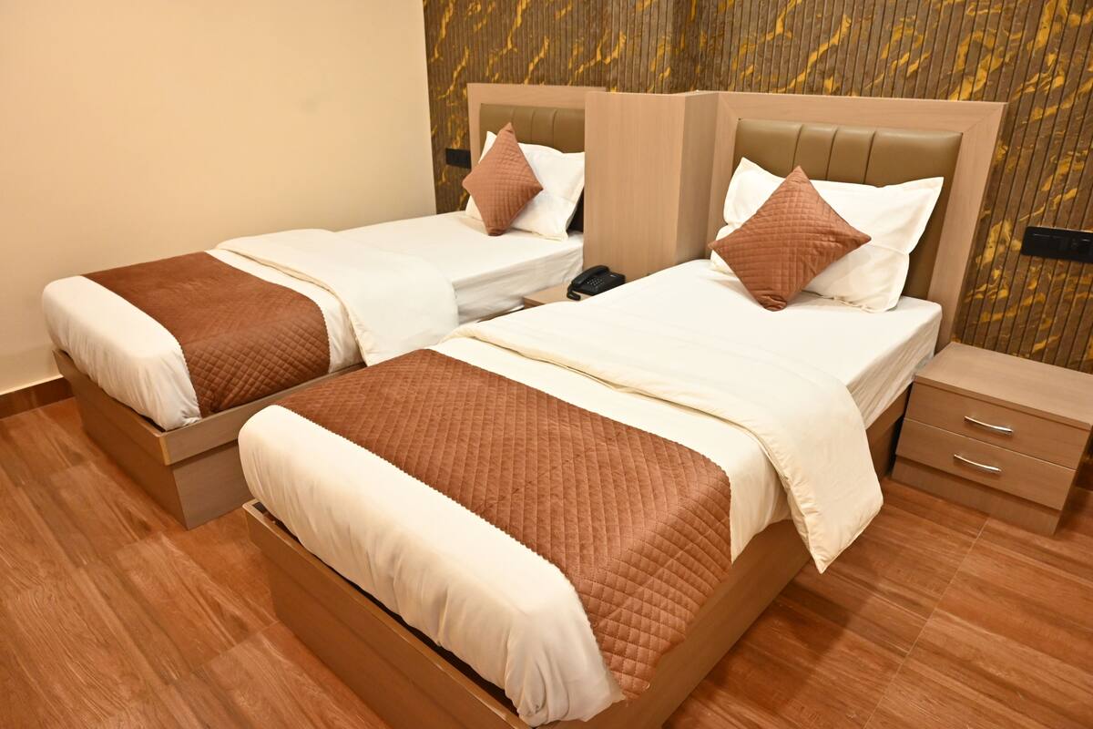 Two twin beds with brown and white bedding, a bedside phone, and a wooden nightstand with drawers.