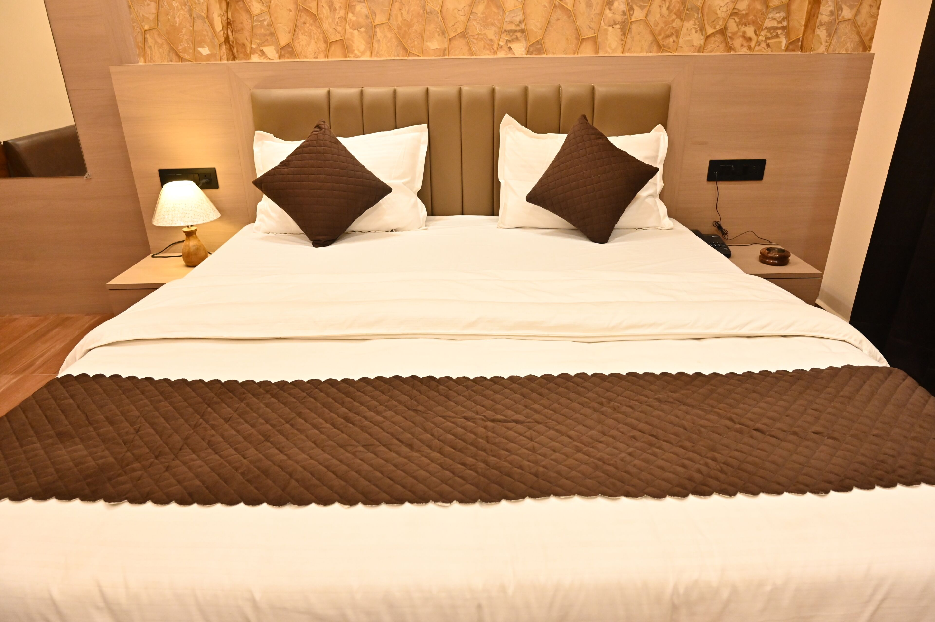 A hotel room with a bed, nightstands, a lamp, and a wall with a textured pattern.