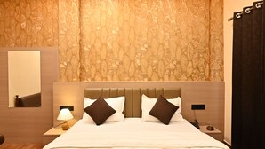 A hotel room with a bed, a nightstand, a lamp, a mirror, and a curtain. - Hotel Pinaka (Pratapgarh)